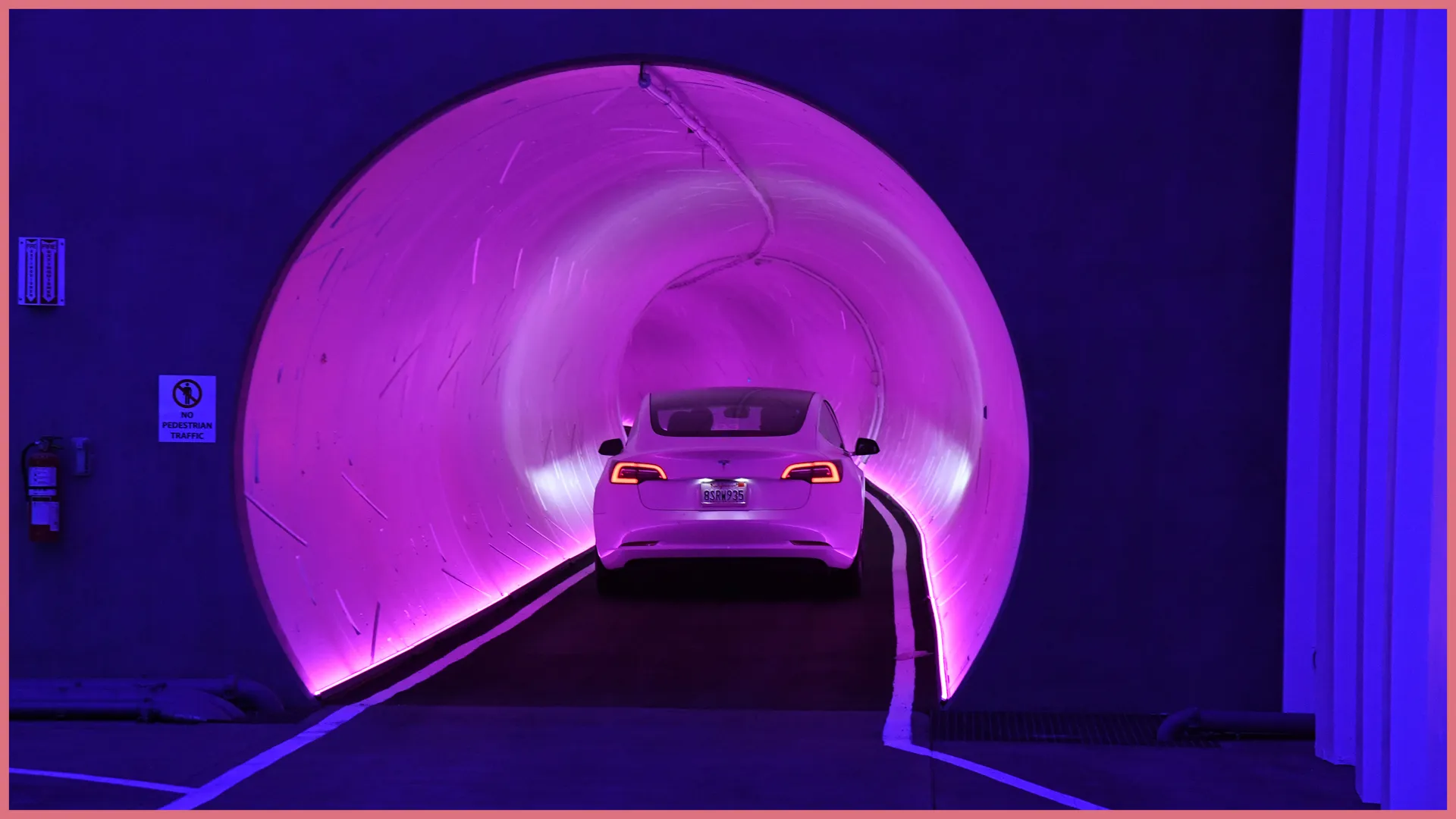 Photograph of a Tesla car driving into a tunnel which is lit in dim purple.